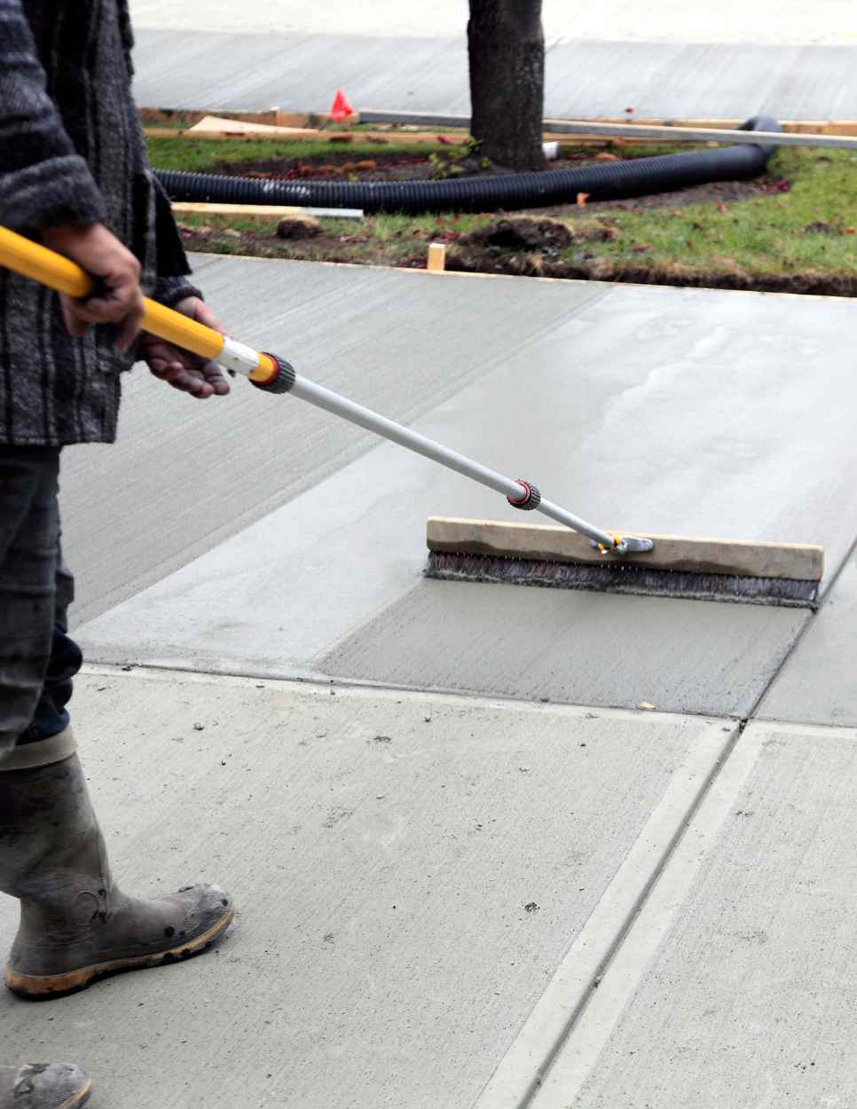 man pushing brush against newly poured and leveled concrete